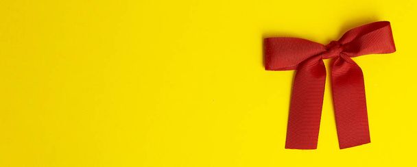 Gift bow on a yellow banner background. Red gift bow with shadow - Φωτογραφία, εικόνα