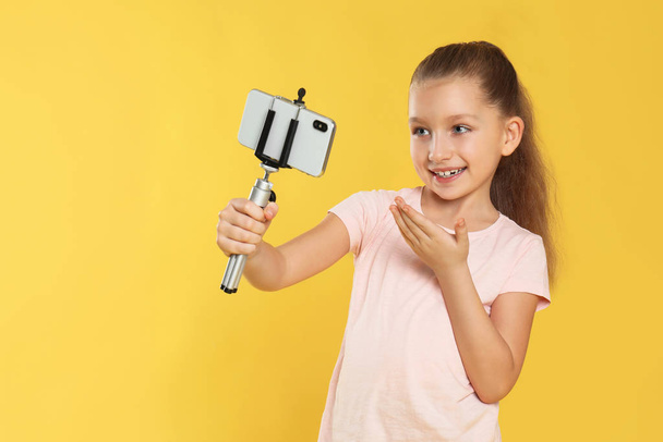 Cute little blogger recording video on yellow background - Foto, Imagen
