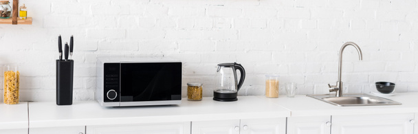 панорамний знімок мікрохвильової печі, електричного чайника, макаронних виробів, ножів і раковини на кухні
  - Фото, зображення