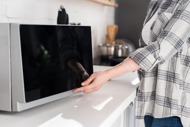 vista cortada da mulher na camisa usando microondas na cozinha
  - Foto, Imagem