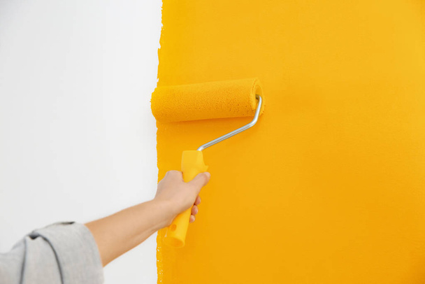 Kobieta malująca białą ścianę żółtym farbą, zbliżenie. Remont wnętrz - Zdjęcie, obraz