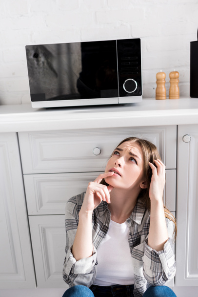 töprengő és vonzó nő nézi mikrohullámú sütő a konyhában  - Fotó, kép