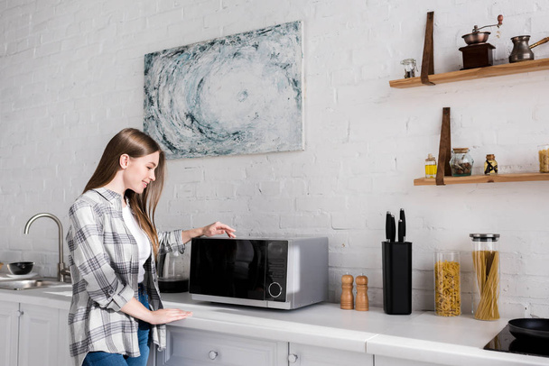 side view of smiling woman looking at microwave in kitchen  - Fotoğraf, Görsel