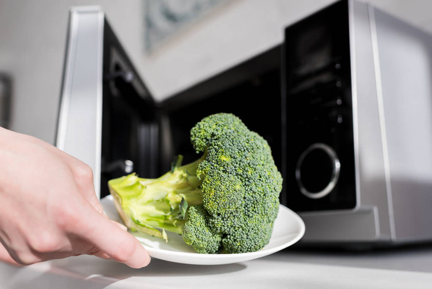 cropped view of woman holding plate with broccoli near microwave  - Fotoğraf, Görsel