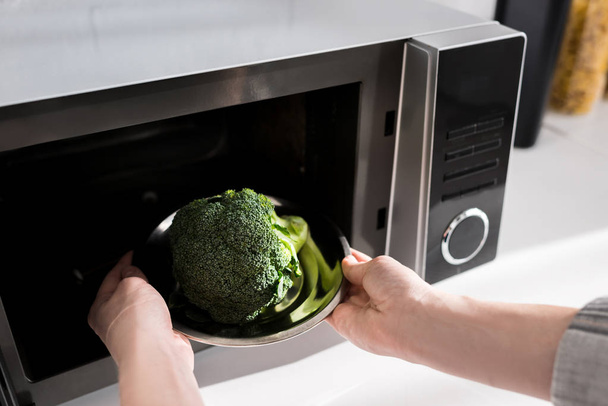 levágott kilátás nő gazdaság lemez brokkoli és üzembe mikrohullámú sütő  - Fotó, kép