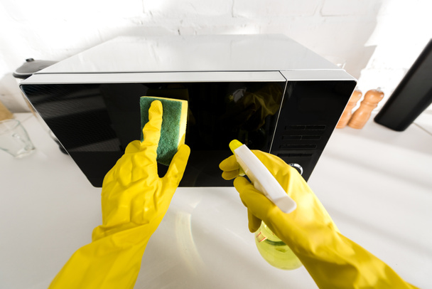 cropped view of woman in rubber gloves cleaning microwave with sponge - 写真・画像