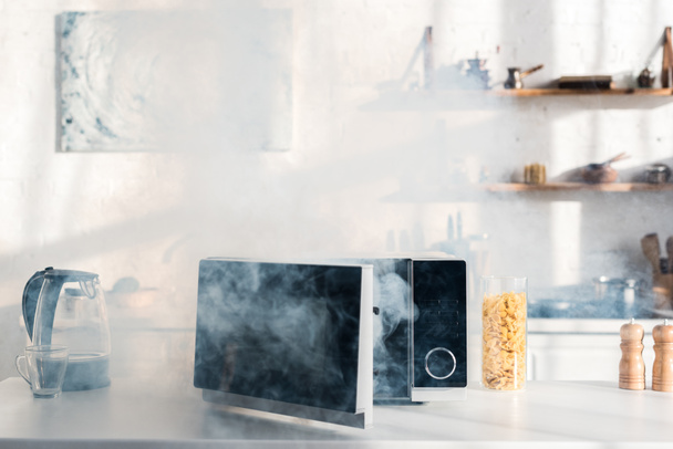 electric kettle, pasta, broken and steamy microwave on table in kitchen  - Фото, изображение