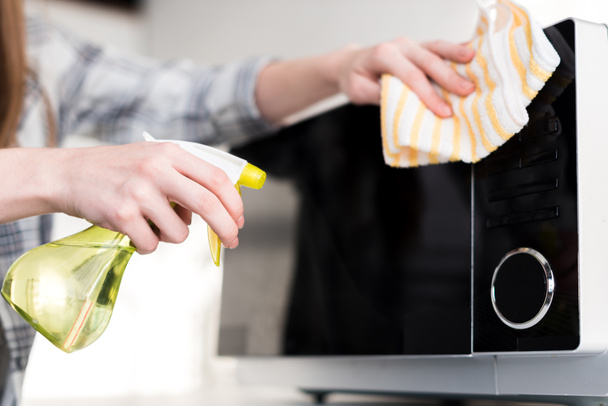 Ausgeschnittene Ansicht einer Frau, die in der Küche Mikrowelle mit Lappen reinigt  - Foto, Bild