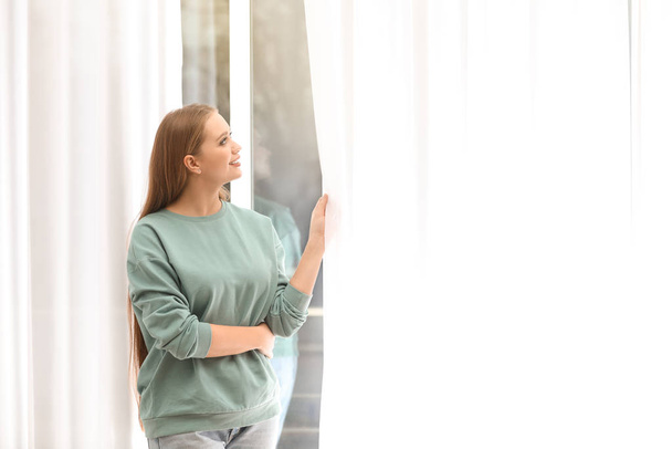 Красивая молодая женщина смотрит в окно дома
 - Фото, изображение
