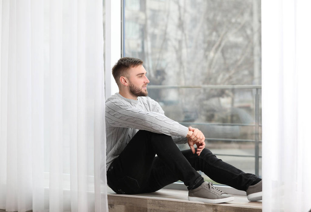 Handsome young man near window at home - Photo, Image