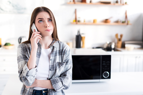 mujer triste hablando en teléfono inteligente cerca de microondas en la cocina
  - Foto, Imagen