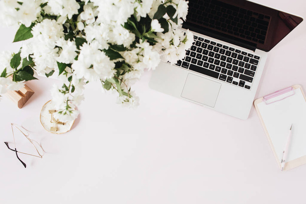 Kantoor bureau met laptop, bloemen boeket en klembord op roze tafel. Flat lat, bovenaanzicht freelancer co-working achtergrond. - Foto, afbeelding