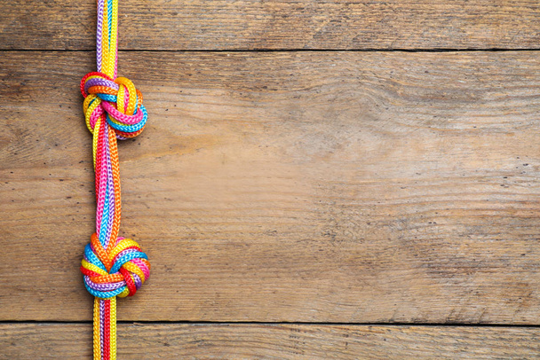 Top view of colorful ropes tied together on wooden background, space for text. Unity concept - Foto, immagini