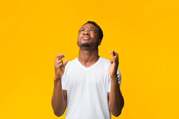 Афроамериканец держит пальцы скрещенными, стоя на жёлтом фоне
 - Фото, изображение