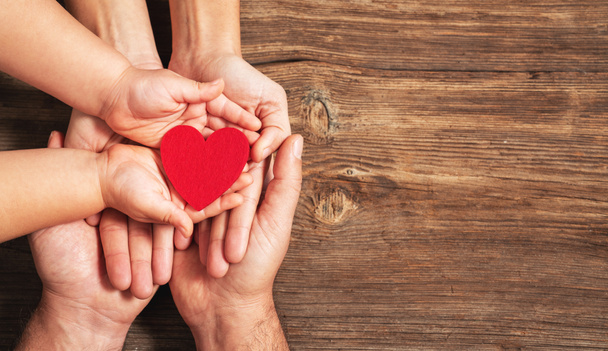 family hands holding red heart on wooden background. Donation, charity, health concept. - Photo, Image