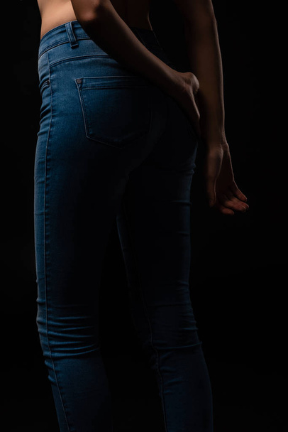 cropped view of sexy young girl in jeans posing isolated on black - Foto, imagen