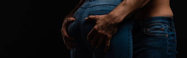 обрізаний вид сексуального молодого чоловіка торкається дівчини сідниці ізольовані на чорному, панорамний постріл
 - Фото, зображення