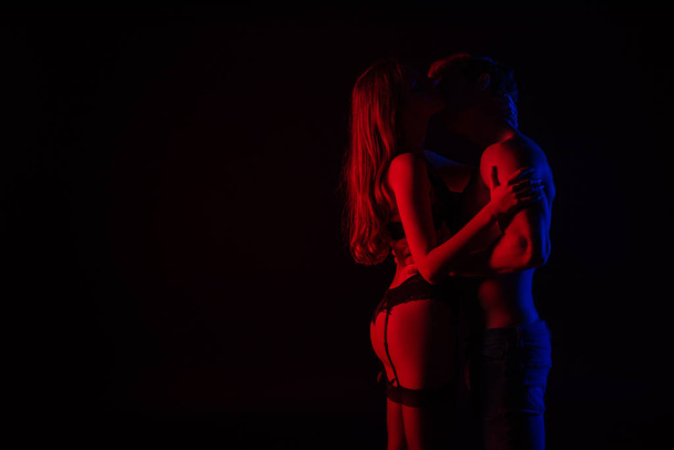 side view of undressed sexy young couple kissing and hugging in red light isolated on black - Photo, Image