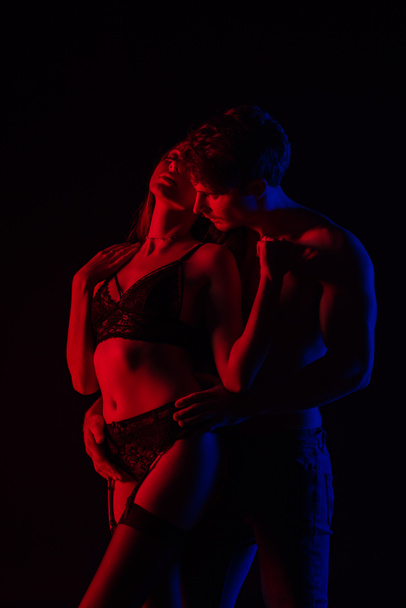 hombre tocando desnuda sexy joven mujer en lencería en luz roja aislado en negro
 - Foto, Imagen