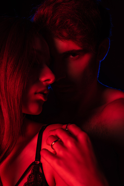 passionate undressed sexy young couple hugging in red light isolated on black - Photo, Image