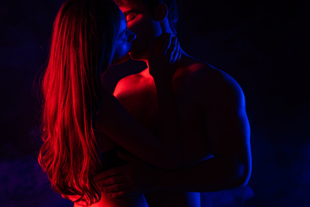 passionate undressed sexy young couple kissing in red light isolated on black - Photo, Image