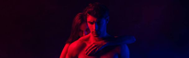 nahý vášnivý sexy mladý pár objímající v červeném a modrém světle na černém pozadí, panoramatický výstřel - Fotografie, Obrázek