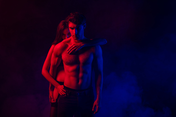 apasionada desnuda sexy joven pareja abrazando en rojo y azul luz sobre fondo negro
 - Foto, Imagen