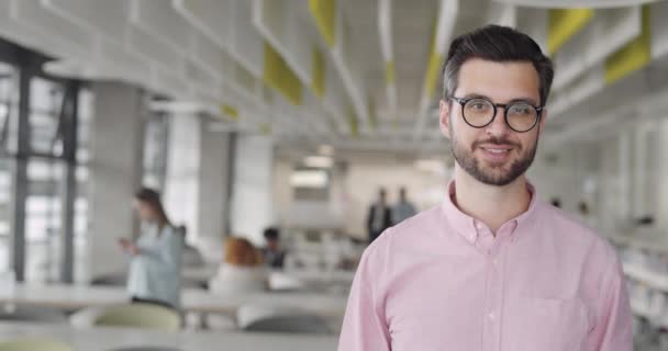 Gözlüklü neşeli erkek ofis çalışanı başını kameraya çevirip gülümsüyor. Mutlu sakallı adam yeni iş sahibi modern çalışma alanında duruyor. İş anlayışı, kariyer, insanlar. - Video, Çekim