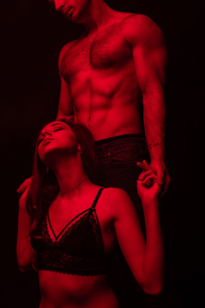 Tutkulu, çıplak, seksi bir adamın kırmızı ışıkta kadınlara dokunuşunun kısmi görüntüsü siyahta izole edilmiş. - Fotoğraf, Görsel