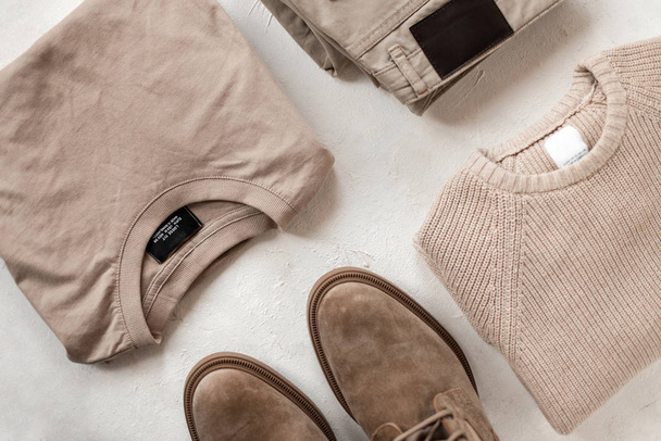 Classic vintage cotton dress shirt with a knit woolen sweater with fashion boots with trendy trousers on the table. Stylish new spring collection of men's clothing and modern shoes. Top view. Close-up - 写真・画像