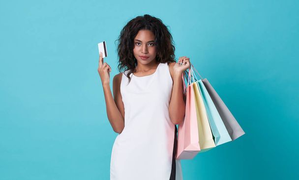 Νεαρή γυναίκα που δείχνει πιστωτική κάρτα και τσάντες ψώνια απομονωμένη σε μπλε φόντο. - Φωτογραφία, εικόνα