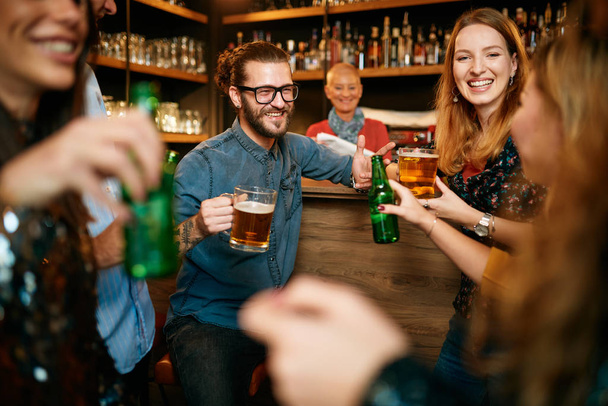 Mała grupa ludzi stojąca w pubie, rozmawiająca, pijąca piwo i ciesząca się piątkową nocą. Noc poza domem. - Zdjęcie, obraz