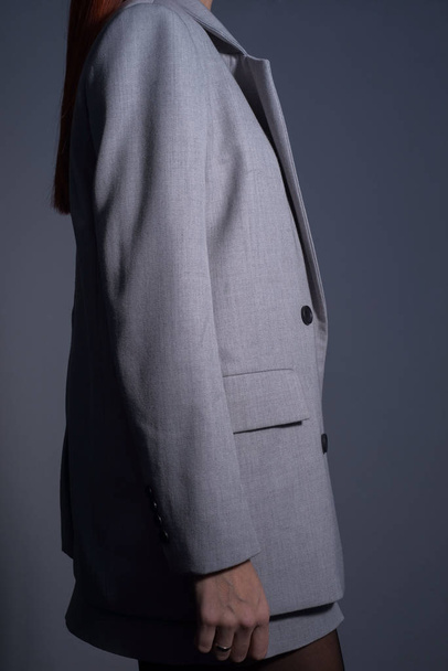 vista lateral, foto para catálogo, chica pelirroja, en una chaqueta de negocios gris, sobre un fondo gris oscuro
 - Foto, Imagen