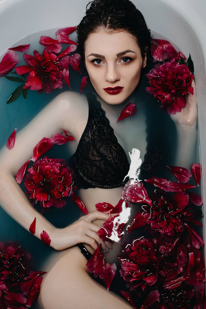 girl with makeup in bra lies and enjoys in bath with peonies - 写真・画像