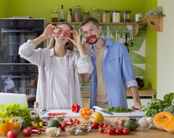 Feliz pareja milenaria divirtiéndose con pimentón fresco y cocinando
 - Foto, imagen