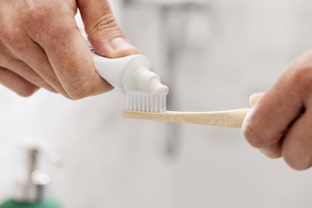man met een bamboe tandenborstel in de badkamer - Foto, afbeelding