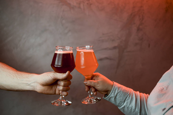 ¡Salud! Primer plano recortado de mujer y hombre dos manos horizontales sosteniendo vasos de cerveza lager
 - Foto, imagen