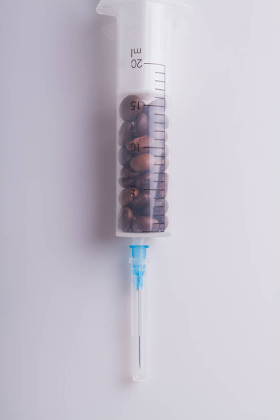 Medical syringe full of coffee beans over white background. - Фото, зображення
