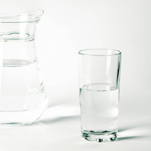 ガラスの中の清らかな水と白い背景の上に立つジャグ - 写真・画像