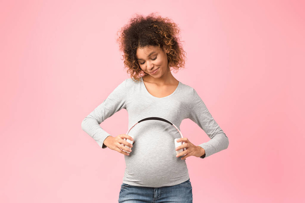 Pregnancy and music. Afro expectant woman holding earphones near belly - Foto, Bild