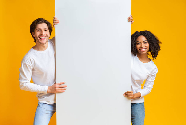 Pareja Interracial feliz sosteniendo tablero blanco grande del anuncio
 - Foto, Imagen