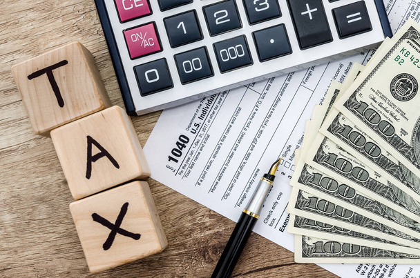 belastingformulier met dollar, rekenmachine en houten blokjes met tekst belasting - Foto, afbeelding