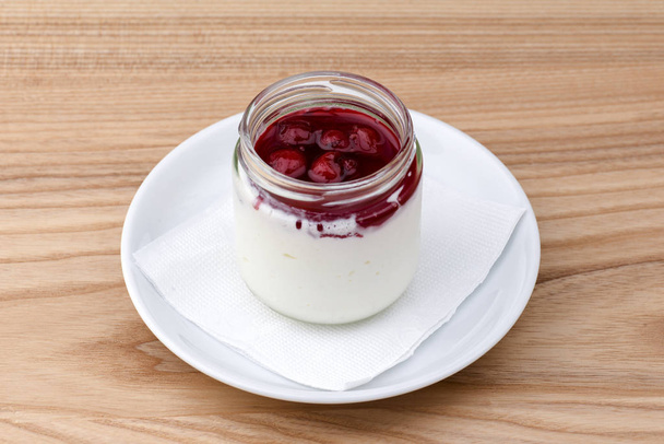 Jelly with berries in glass jar. Italian dessert panna cotta on light wooden table. - Fotoğraf, Görsel
