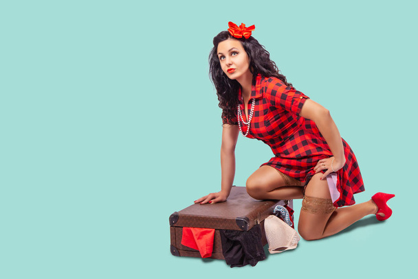 junge Frau sitzt auf dem Boden und legt Kleidung in einen Koffer - Foto, Bild