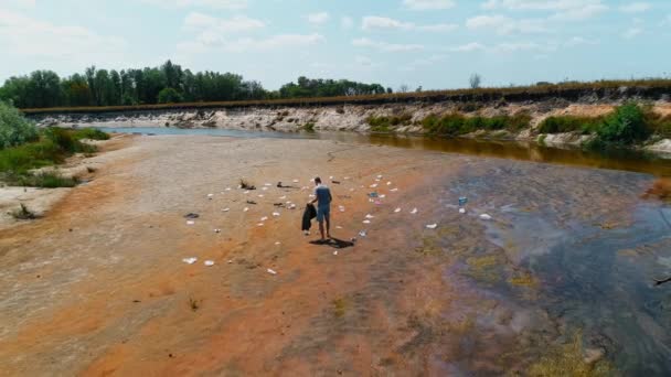 Aerial view of man who collects plastic trash on the banks of polluted river - Footage, Video