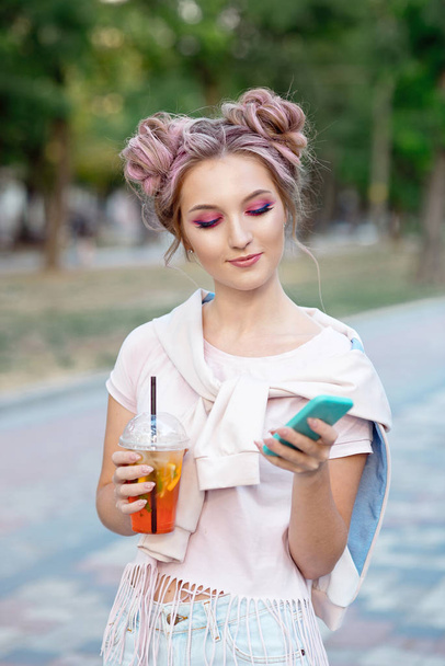 Happy cheerful young blonde with pink hair, walks against the backdrop of the city, calls on a mobile phone to his friends. Blonde student is resting on the street after college to meet friends - Photo, Image