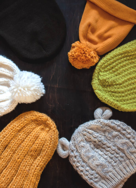 Different types of knitted hats yellow, green, white, gray on a dark wooden background with copy space. View from above - Photo, Image