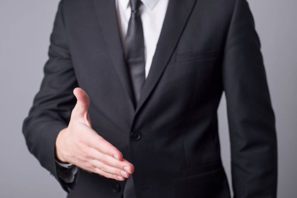 Portret van een man in een zakenpak die zijn hand uitsteekt voor een handdruk. Minimalistisch bedrijfsconcept. Op een grijze achtergrond. - Foto, afbeelding
