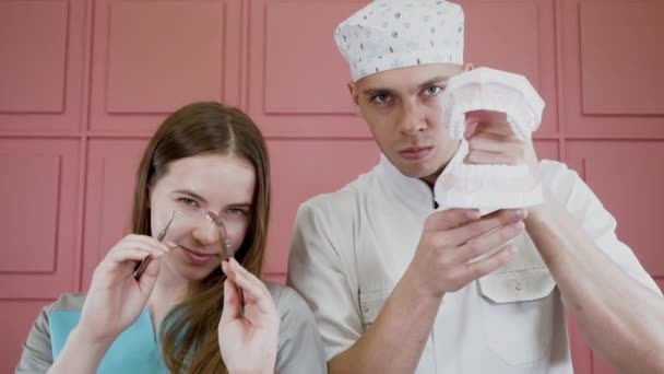 Retratos de duas pessoas em uniforme médico posando com ferramentas dentárias e mandíbula
 - Filmagem, Vídeo