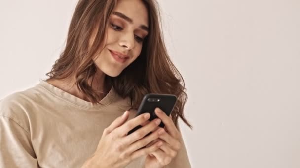Smiling beauty brunette woman using smartphone and enjoying this moment over grey background - Filmagem, Vídeo